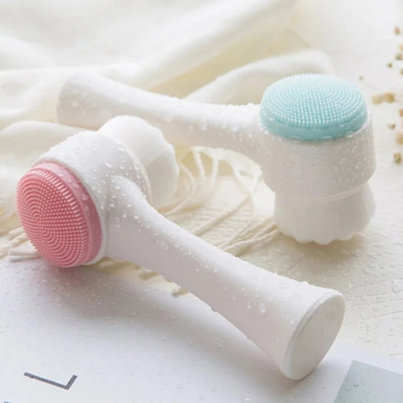 Two silicone face cleaning brushes, one pink and one white with a blue head, on a textured surface.