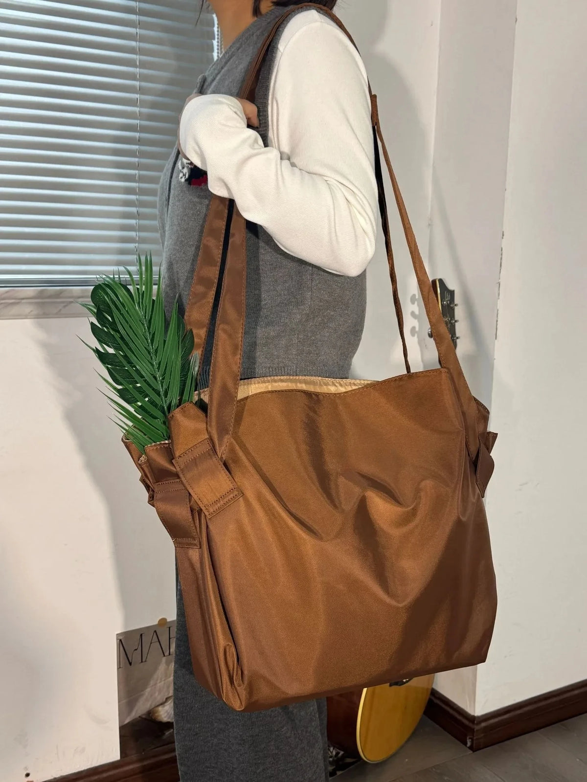 Person holding a brown shoulder bag with a plant, standing indoors.
